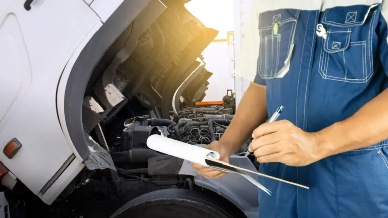 Um mecânico de macacão azul anota com atenção em uma prancheta enquanto verifica o motor aberto de um caminhão durante uma manutenção preventiva.